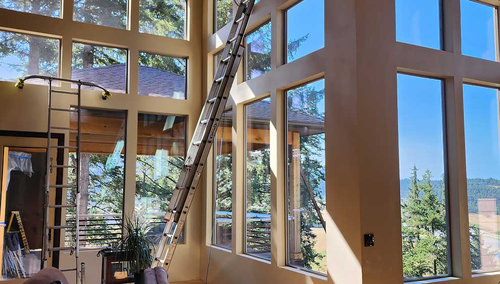 Floor-to-ceiling great-room windows with ladder and forest light